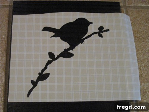 Close-up view of a delicate bird stencil made from contact paper, being carefully peeled from its backing