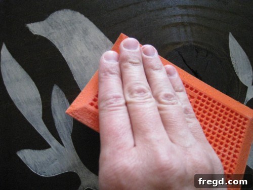 Carefully peeling the contact paper stencil from the charger, revealing the crisp, painted bird design underneath