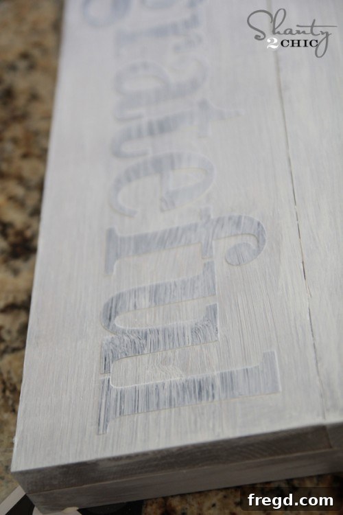 Applying thin coat of paint over stencil letters on wood sign