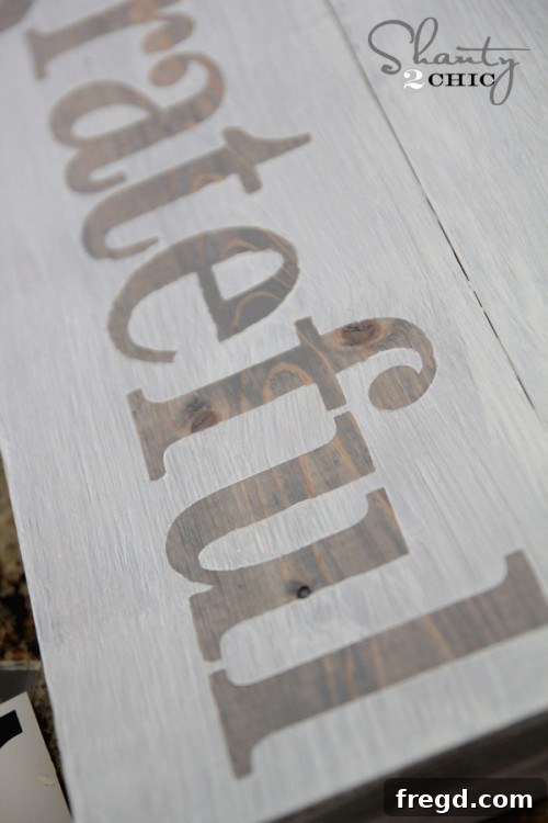 Distressing the completed wood sign with sandpaper for a vintage and aged look