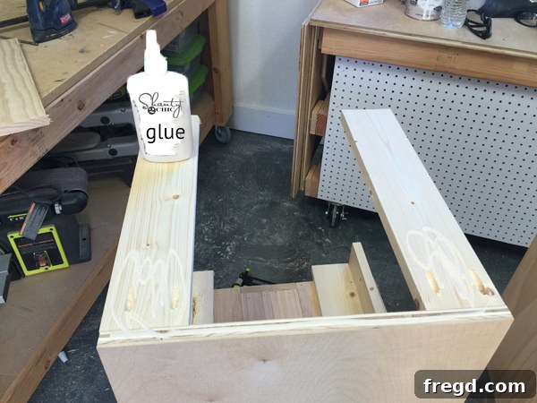 Build Your Own Rolling Storage Ottoman Coffee Table 11 Close-up of wooden planks being attached to the side of an ottoman using wood glue and an 18-gauge nailer, ensuring a flush and secure fit.