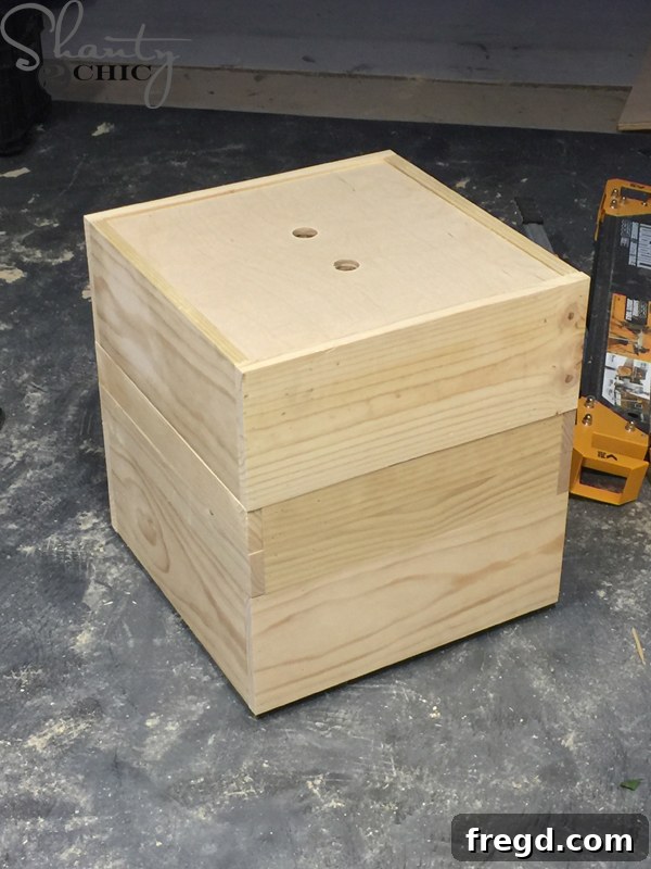Build Your Own Rolling Storage Ottoman Coffee Table 17 A wood drill with a 1-inch hole saw attachment in use, drilling finger holes into the wooden top of an ottoman for easy lid removal.