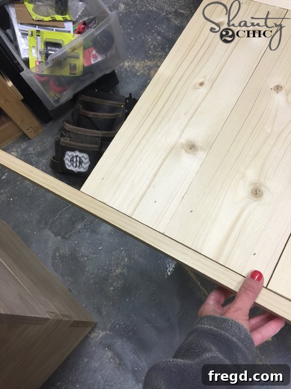 Build Your Own Rolling Storage Ottoman Coffee Table 30 A hand holding a 1x2 wooden trim piece against the edge of a patterned tabletop, marking it for a precise cut.