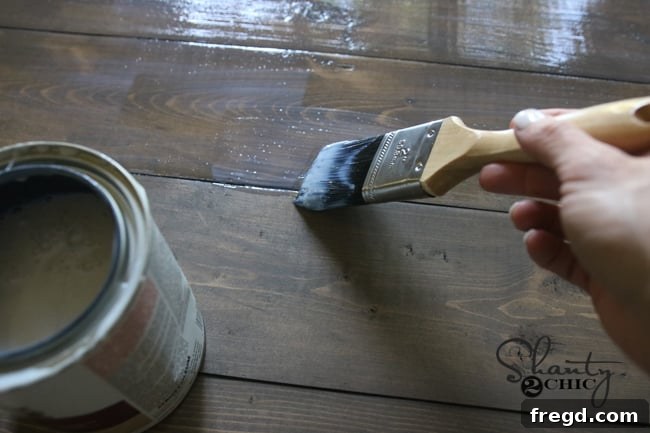 Build Your Own Rolling Storage Ottoman Coffee Table 34 A close-up view of a brush applying a clear, thick coat of polyurethane finish to a wooden surface, showing its protective quality.