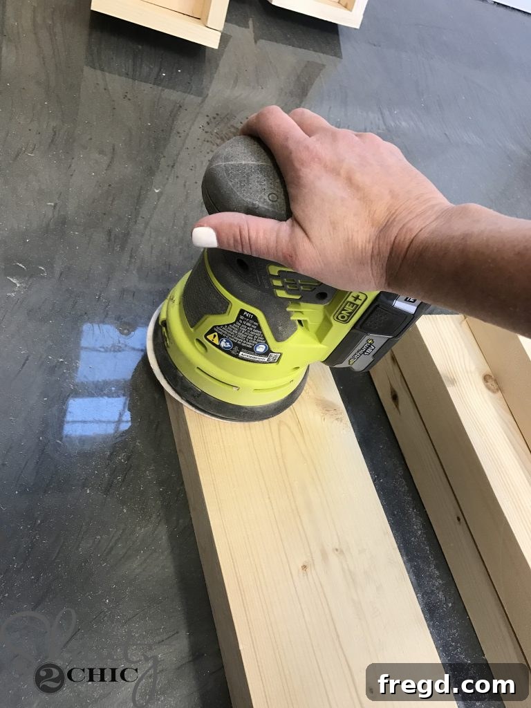 Detailed shot of a hand sanding a 2x6 wooden board, preparing its surface for a smooth finish on the DIY lounge chair project.