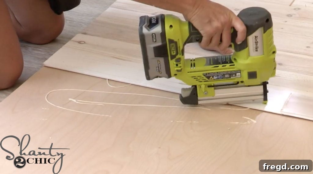 Installing the bottom trim piece of the barn door, creating a complete border with wood glue and brad nails.