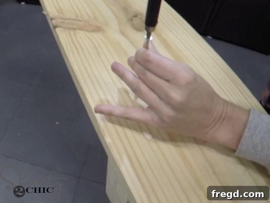 A horizontal base plank being attached to the bottom end of the vertical leg assembly using wood glue and screws, viewed from below.