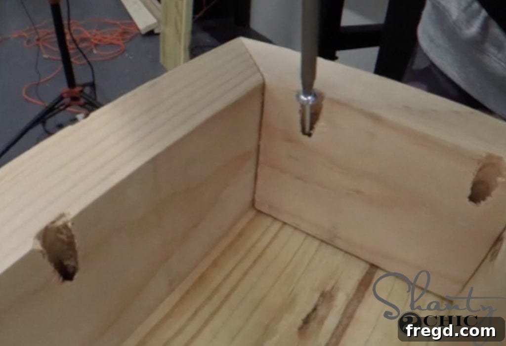 The console table flipped upside down, showing one apron being centered and attached to the bottom of a base plank using pocket hole screws and wood glue.