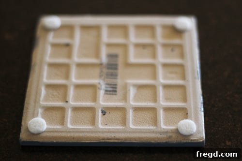 A hand pressing a felt pad onto the corner of a newly finished DIY coaster.