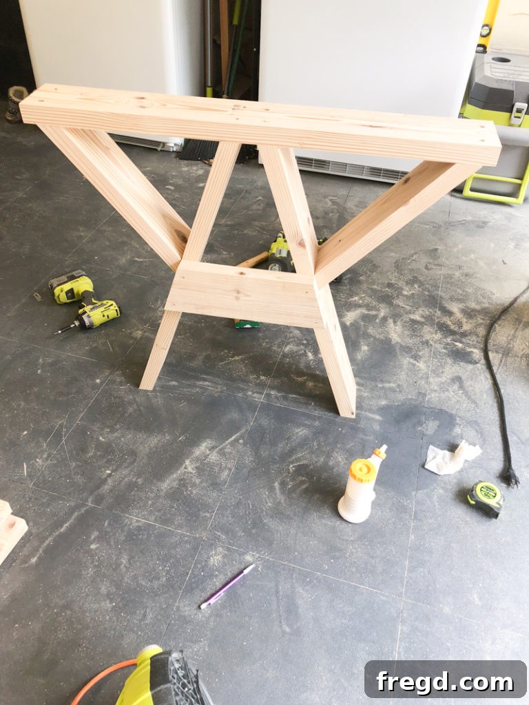 Sawhorse Chic: A DIY Modern Farmhouse Dining Table 19 A leg brace being nailed into place on a sawhorse table base