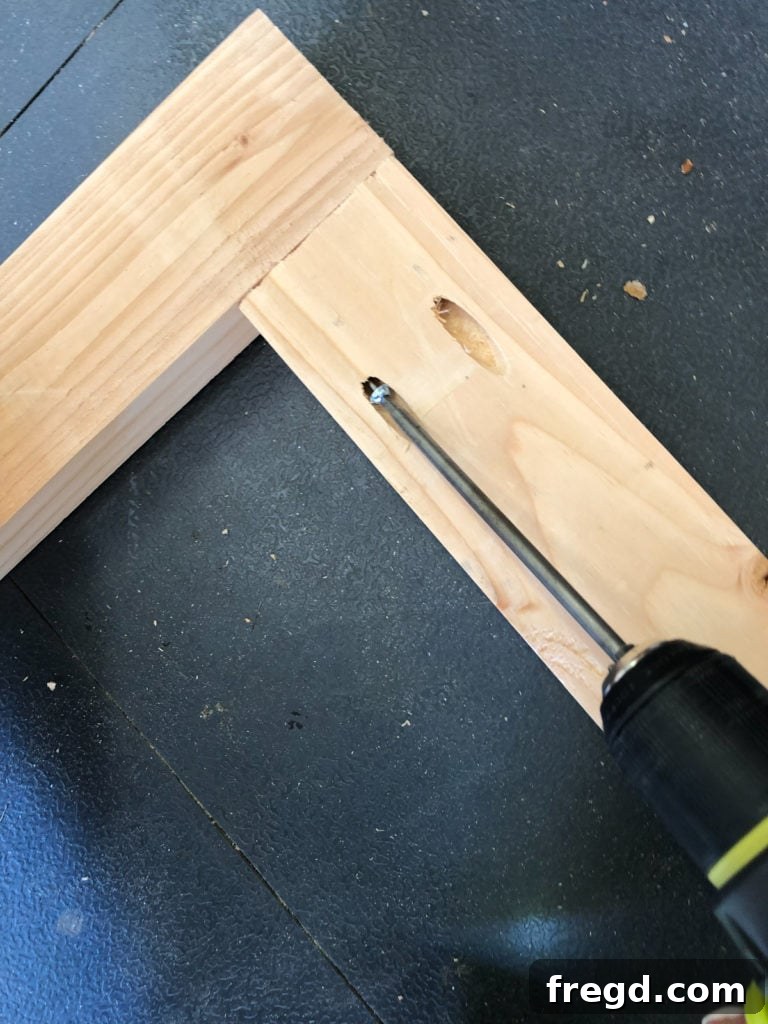 Attaching vertical frame pieces to the bottom horizontal board using pocket hole screws, forming the front panel