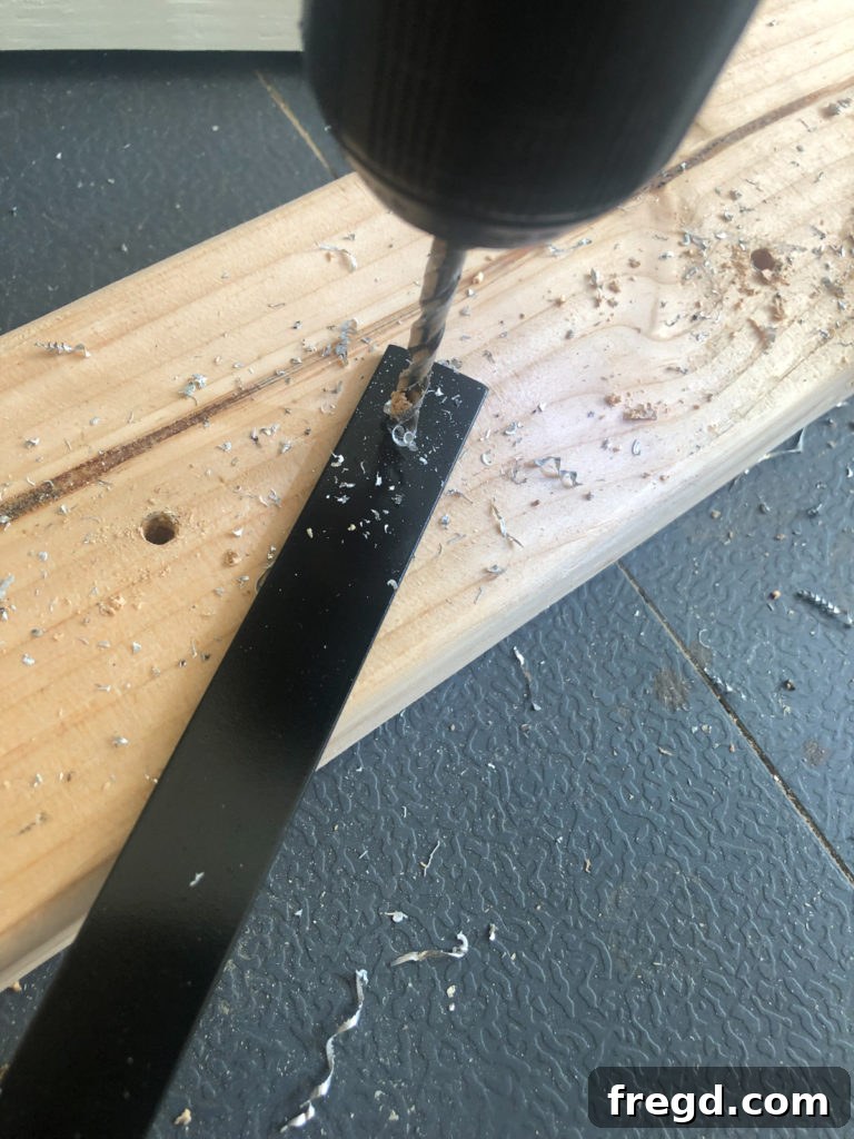 Drilling pilot holes into the ends of a black-painted aluminum flat bar for the crate's enclosure