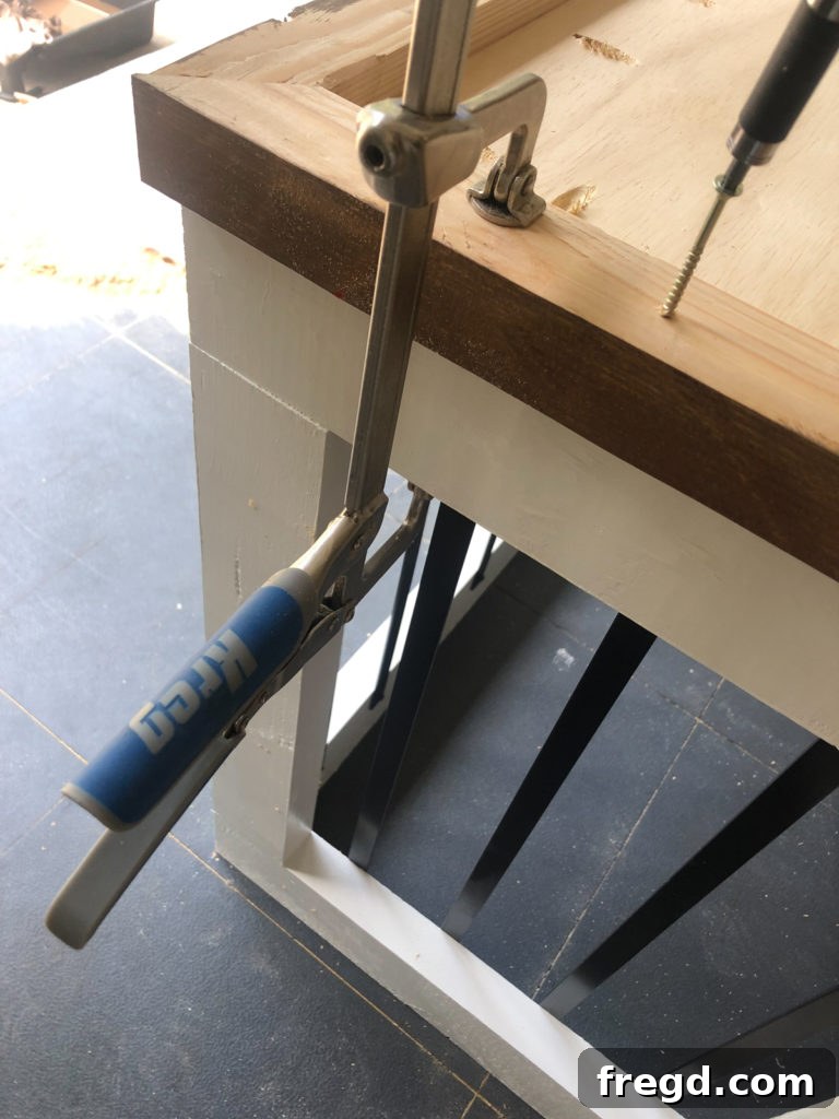 Attaching the wooden base to the inverted dog crate assembly using wood glue and 2.5-inch wood screws