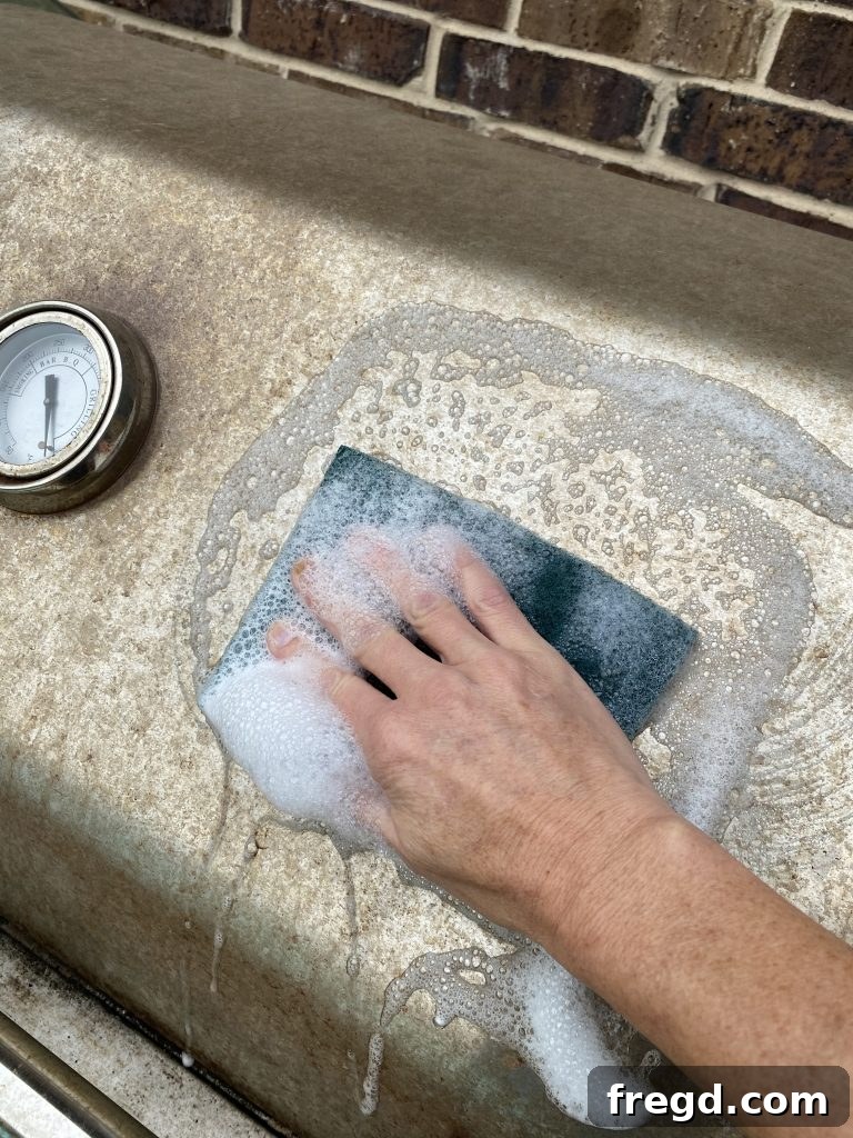 Transform Your Rusty Grill: Paint It Like New 3 Close-up of a hand scrubbing a rusty grill surface with a scouring pad, soap, and water during the cleaning process.