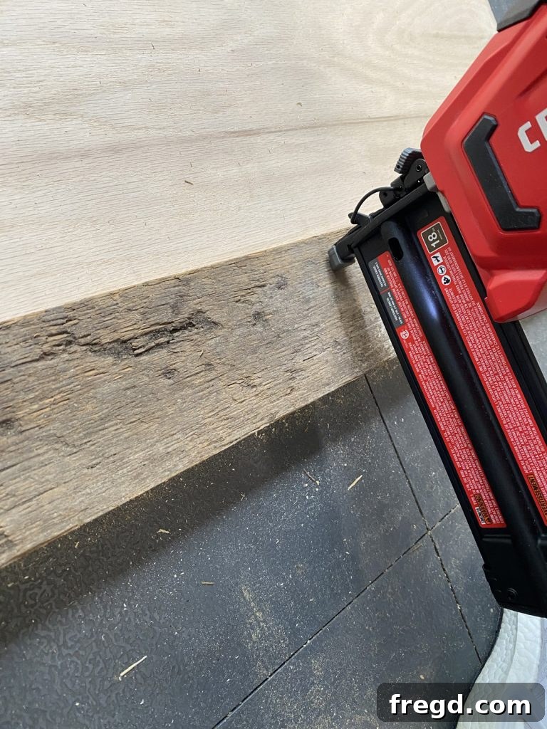 Close-up of attaching barn wood strips to a plywood base with wood glue and brad nails.