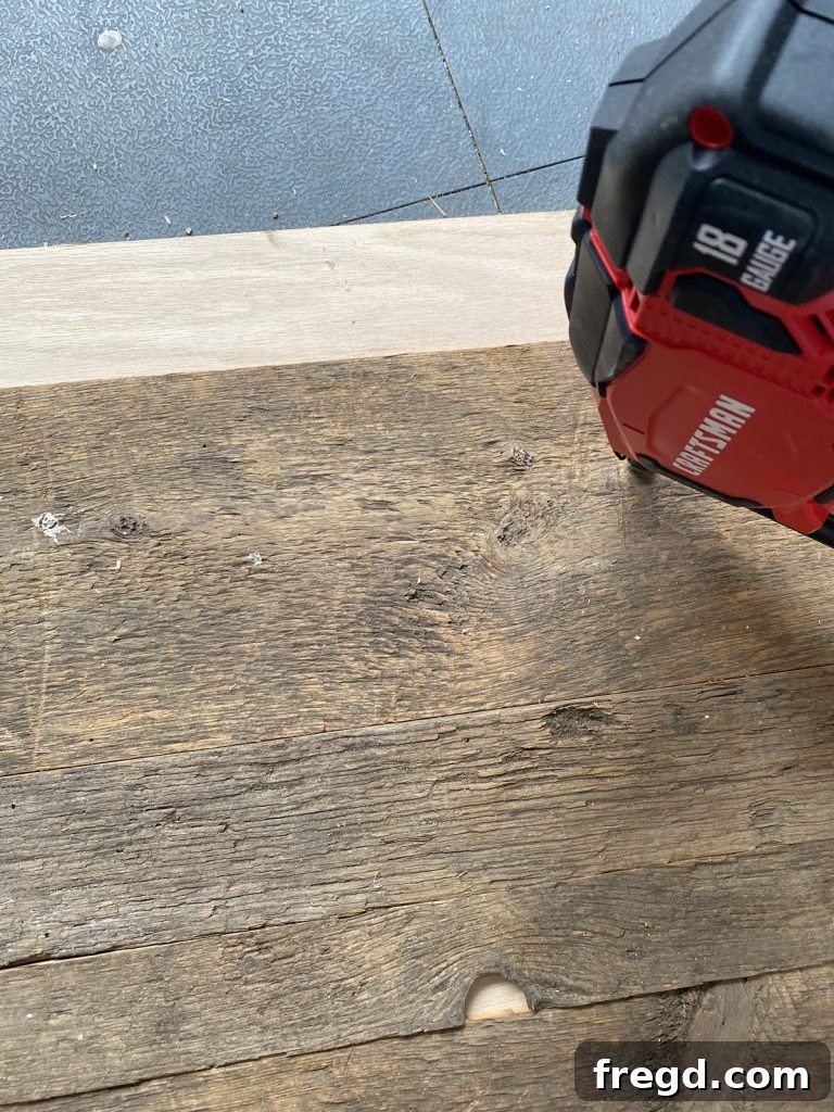 Mid-project view showing several rows of barn wood securely attached to the plywood.