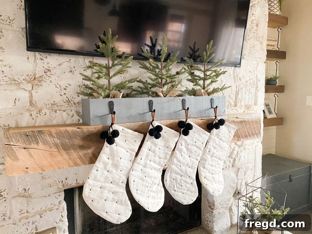 The finished DIY stocking holder with hooks attached, filled with mini Christmas trees, and displaying holiday stockings.