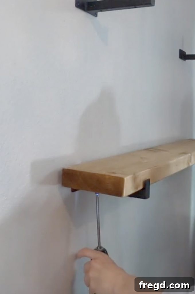 Inexpensive DIY Wall Shelves 13 Securing a stained wood shelf board to a wall bracket with screws