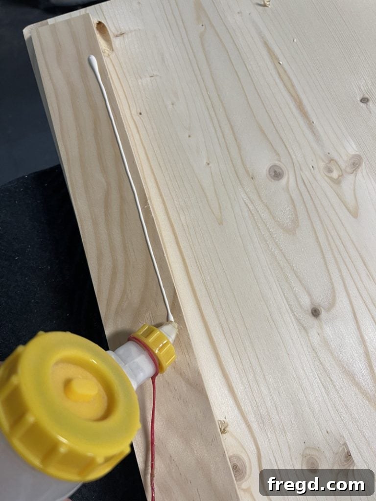 Applying a bead of wood glue along the edge of a tabletop, preparing to attach a trim piece.
