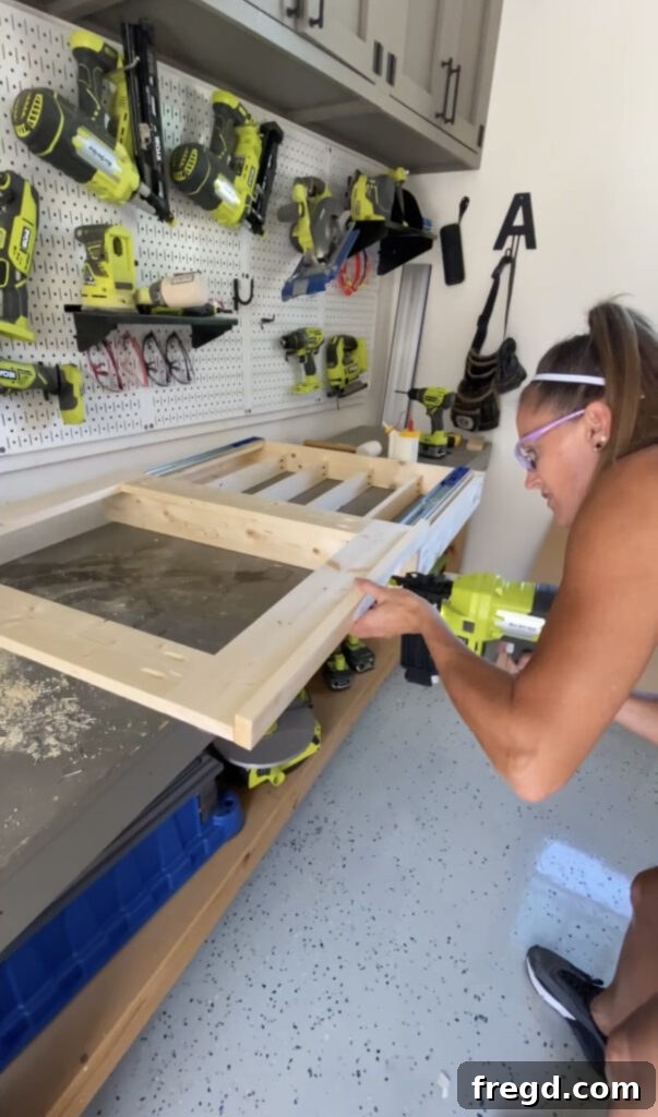 Elevate Your Bathroom with DIY Mirrored Storage 12 Demonstrates attaching the bottom trim piece to the mirror frame using brad nails.