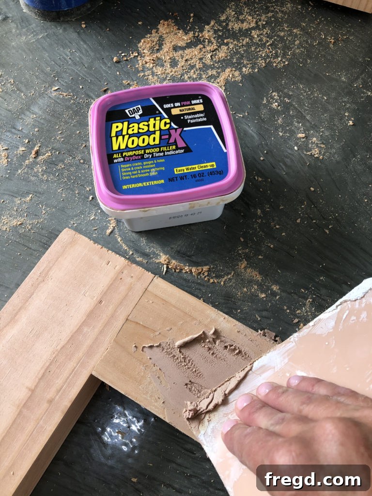 Elevate Your Bathroom with DIY Mirrored Storage 14 Close-up view of wood filler being applied to imperfections and nail holes on a wooden surface.