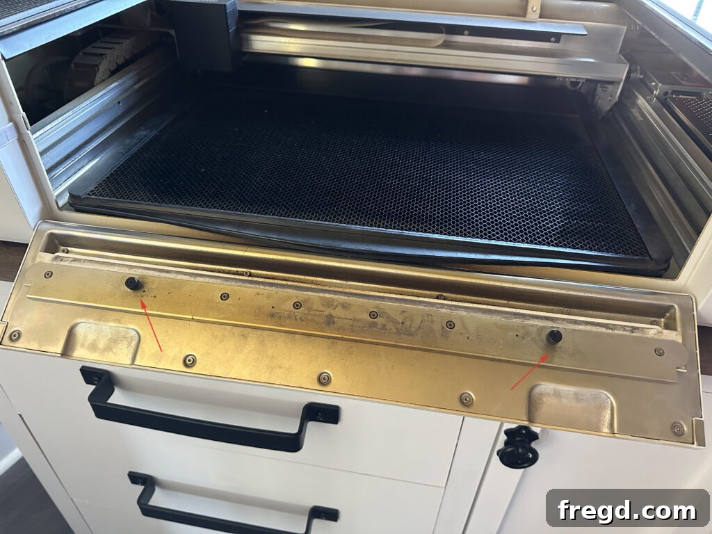 Close-up of the front plate screws on a Glowforge Pro, indicating where to loosen for passthrough slot access.
