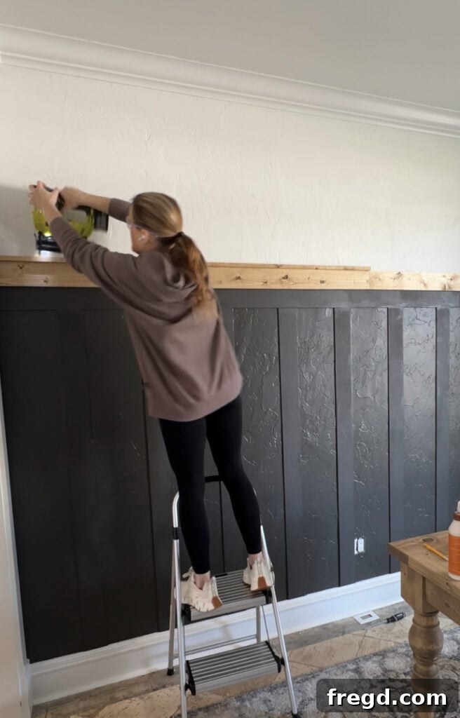 Transform Your Home with DIY Board and Batten Paneling 16 The final stained 1x2 wood trim piece being added on top of the 1x4, completing the layered decorative cap of the board and batten.