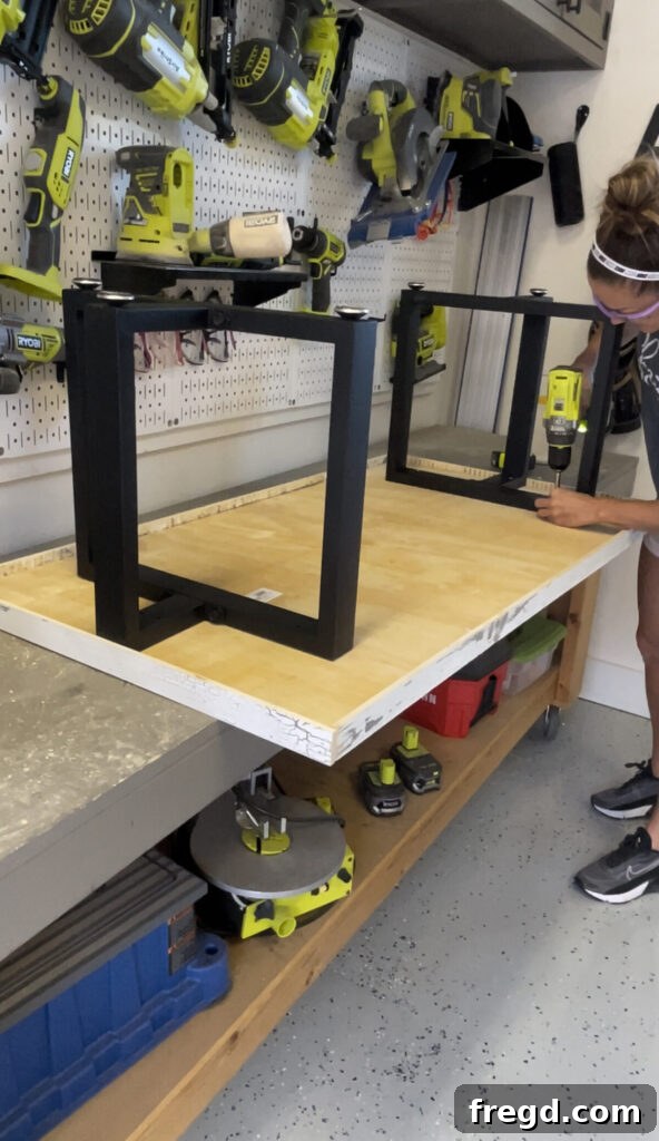 The finished coffee table top flipped upside down, with black metal legs being positioned and attached to the plywood base.