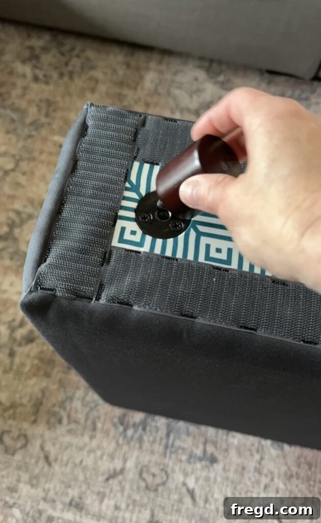 A hand twisting a wooden foot into the pre-drilled hole on the bottom of a Lovesac Sactional base.