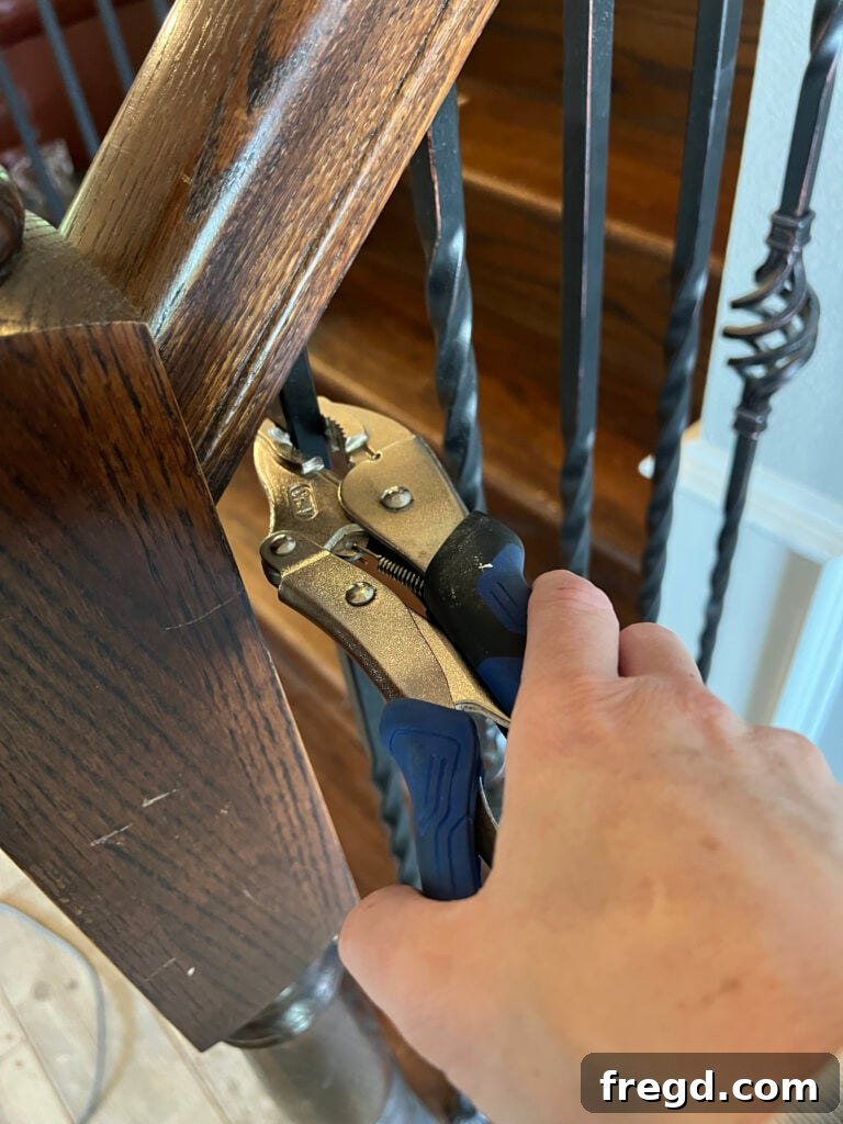Close-up of a hand using vise grips to remove an old baluster from the handrail.