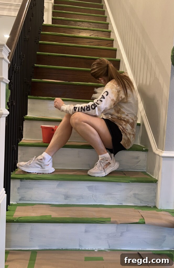 Painting the stair risers white with careful taping to protect the stained treads.