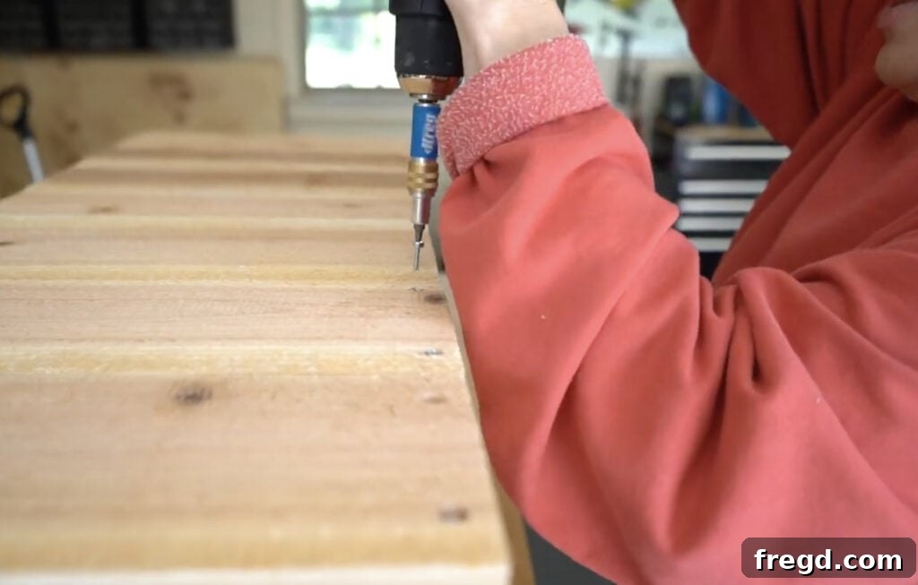 Attaching short cedar slats to the side of the planter frame using wood screws and glue, ensuring flush edges.