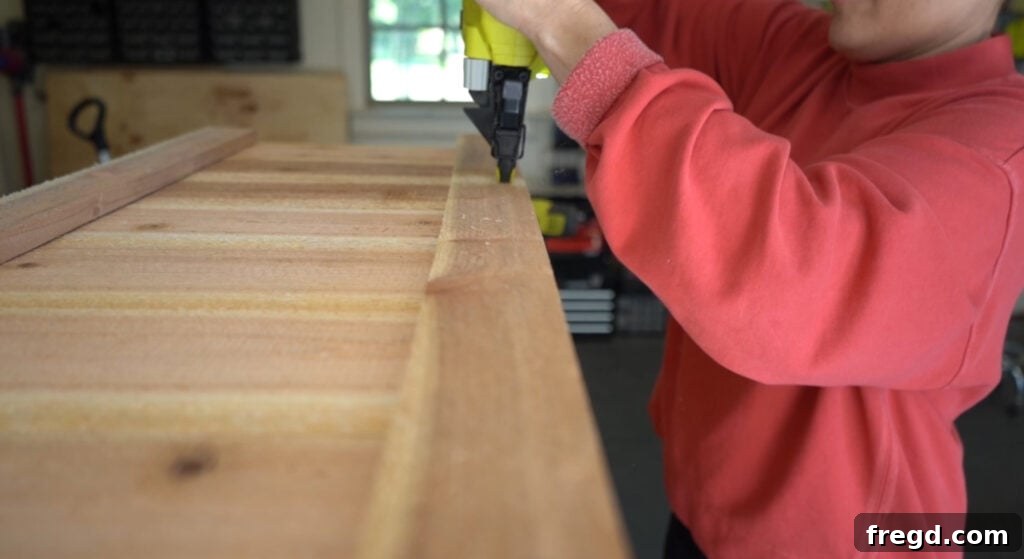 Attaching the first set of side trim pieces to the short sides of the planter box using brad nails and wood glue.