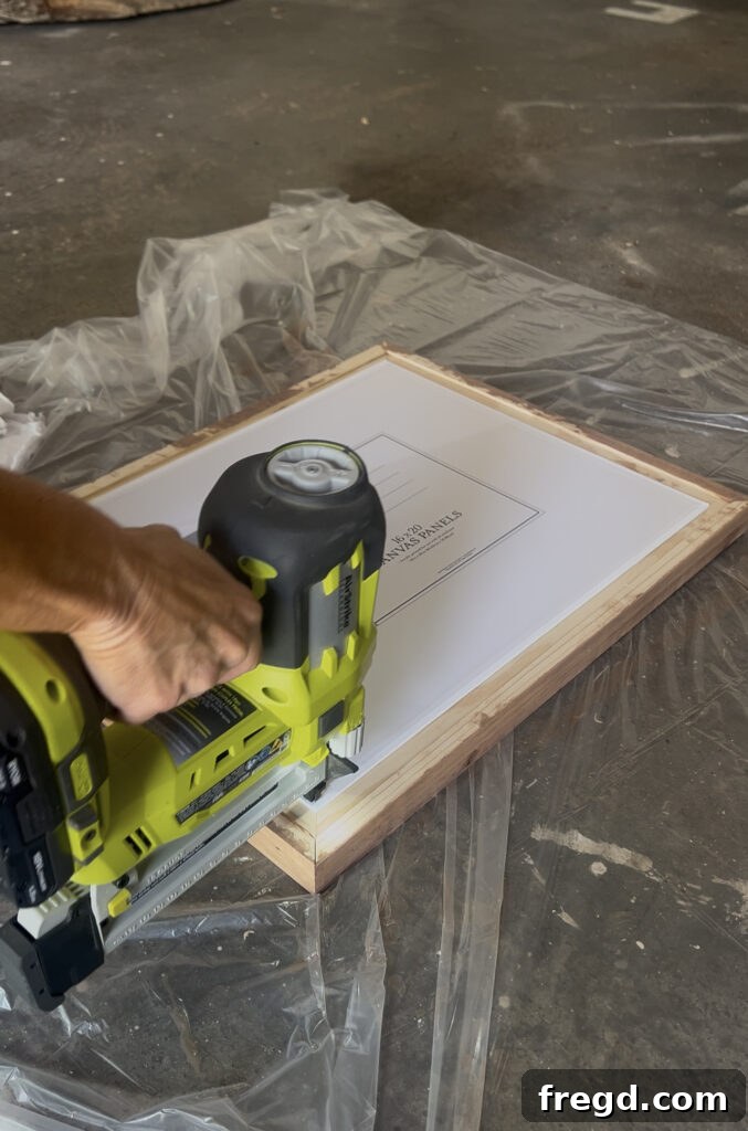 A canvas panel being placed into the back of a stained wooden frame, fitting snugly into the created lip.