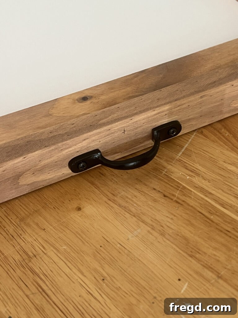 Close-up of a decorative black drawer pull securely attached to the top of a stained wooden frame.