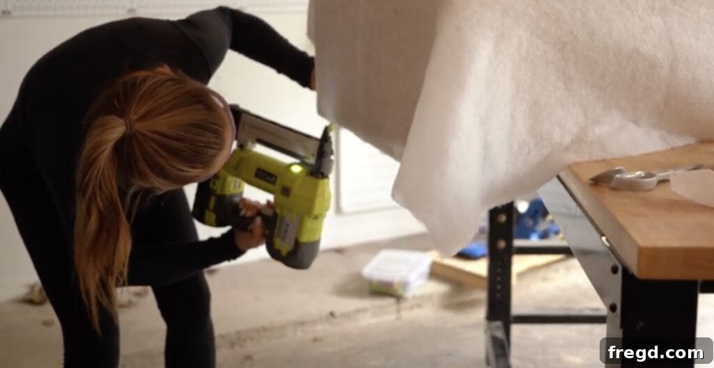 Tacking batting securely to the bottom edge of the plywood sides, preparing the bench for its luxurious cowhide upholstery.