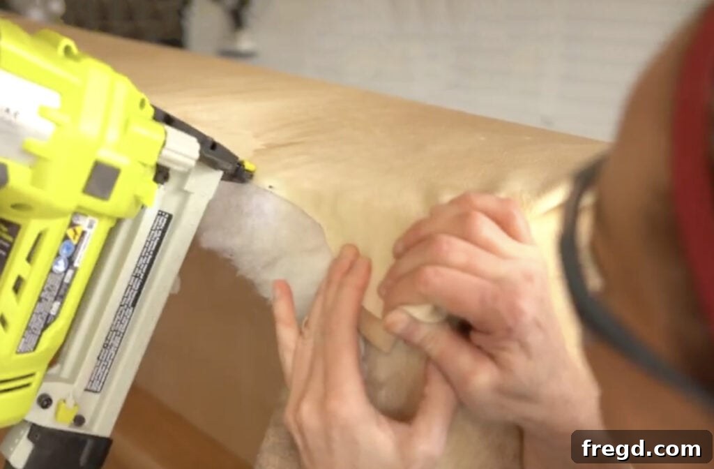 Securing the meticulously folded cowhide corner to the bottom edge of the plywood, ensuring a clean and durable upholstery finish.